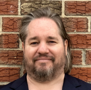Photo of Andrew Woods, a blue-eyed handsome man. has brown hair with a touch of gray